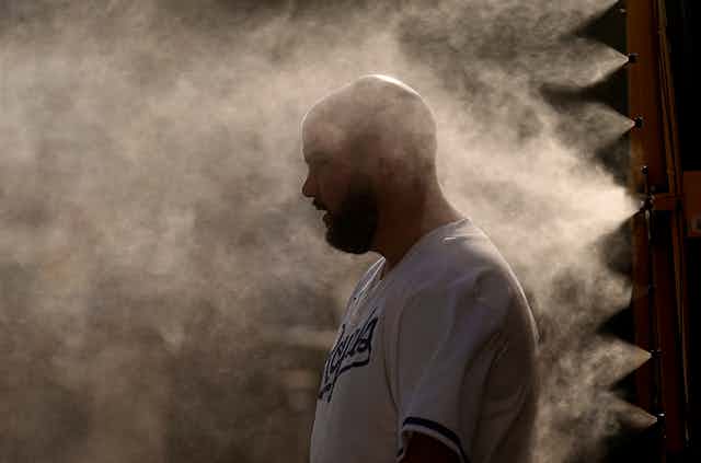 A man looks overheated as he stands by jets blowing cool mist.