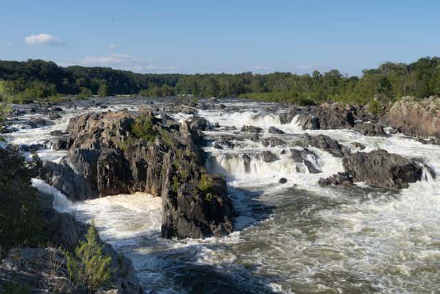 A river runs over and around large rock formations, with water foaming and churning