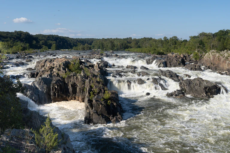 A river runs over and around large rock formations, with water foaming and churning