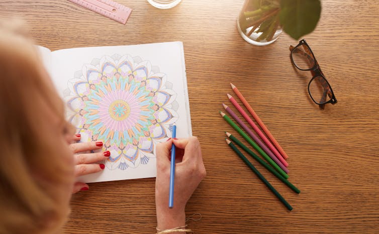 A woman colours in a colouring book.