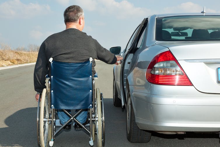 Man who is a wheelchair user next to his car.