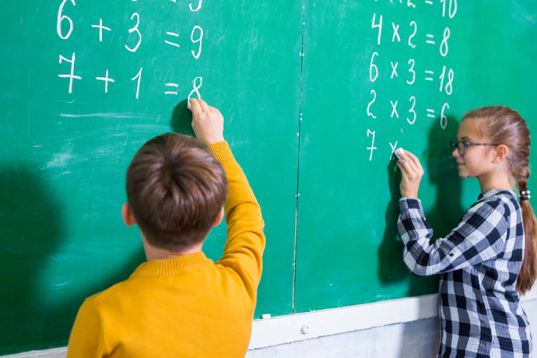 Des enfants écrivant des additions et des multiplications sur un tableau noir dans une classe