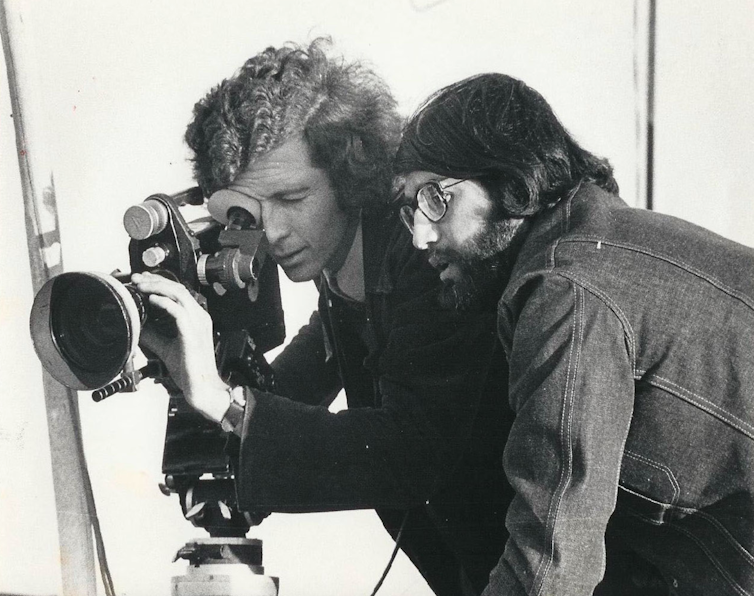 Two men looking down the lens of a film camera in the 1970s.