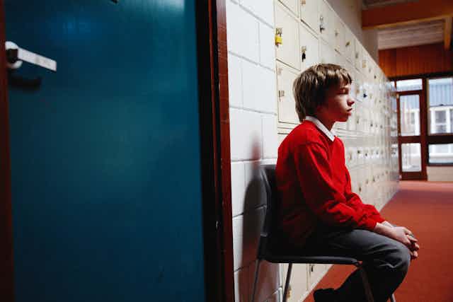 Student sits on chair in school corridor