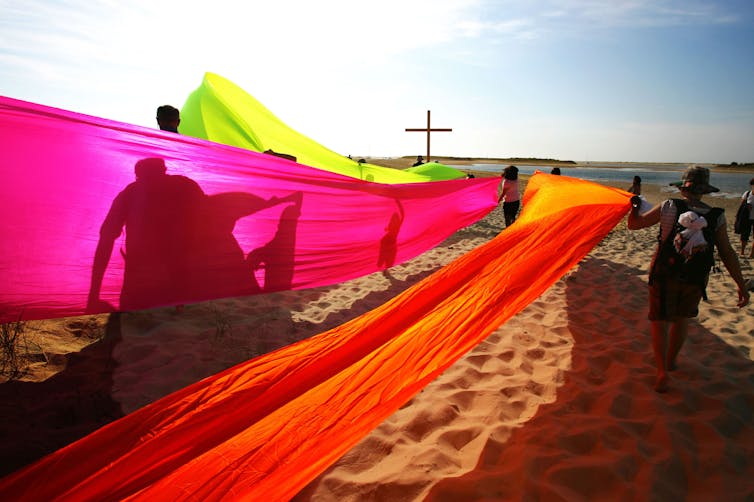 People with flags and a cross on a beach.