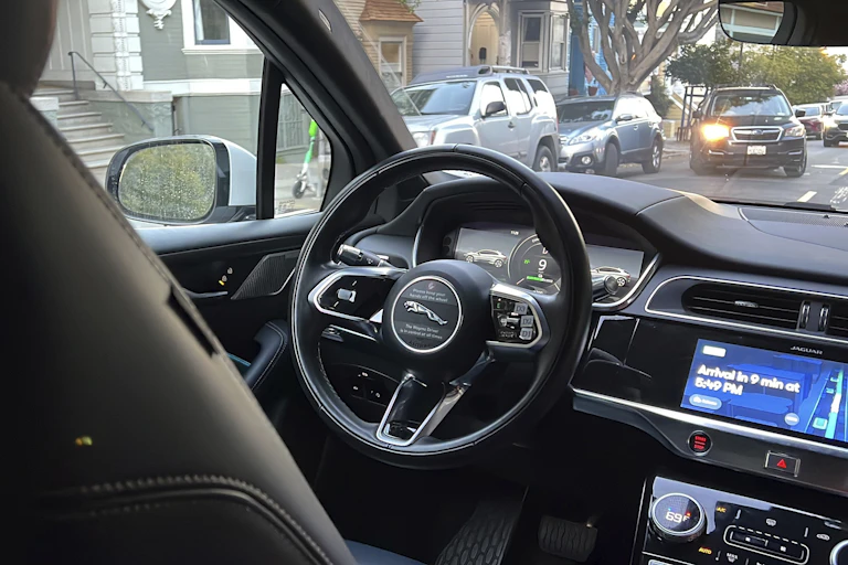 view from the backseat of a car driving on a city street with no one in the driver seat