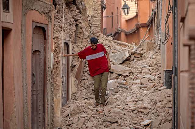 A man walks carefully through a narrow street filled with broken masonry from buildings.