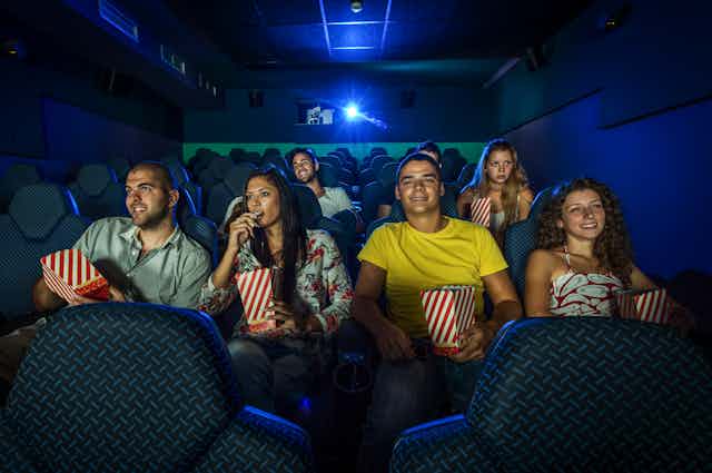 A group of moviegoers munching on popcorn watch a film.