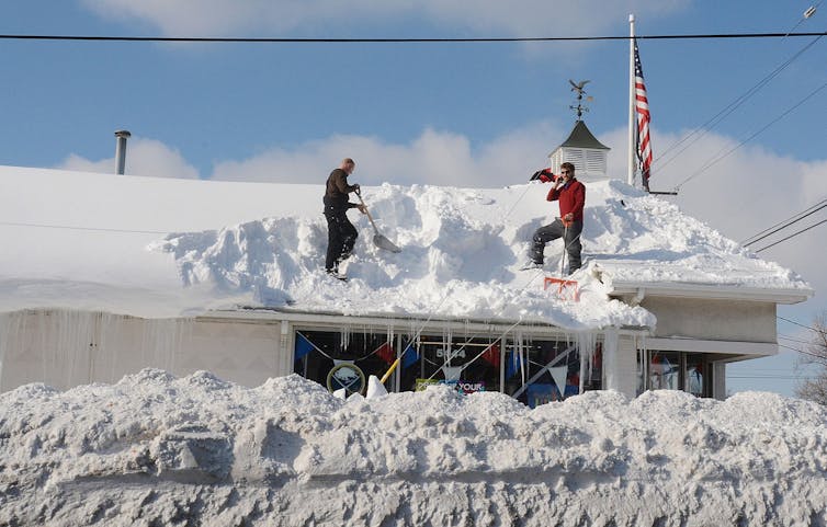 Dos personas retiran nieve de un tejado hasta las rodillas