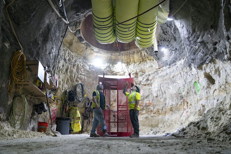 Trabajadores en una caverna subterránea observan un enorme agujero en el techo y una tubería.