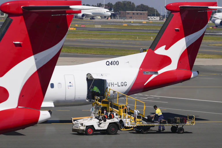 Baggage handlers move suitcases from a trolley into the hold of a plane