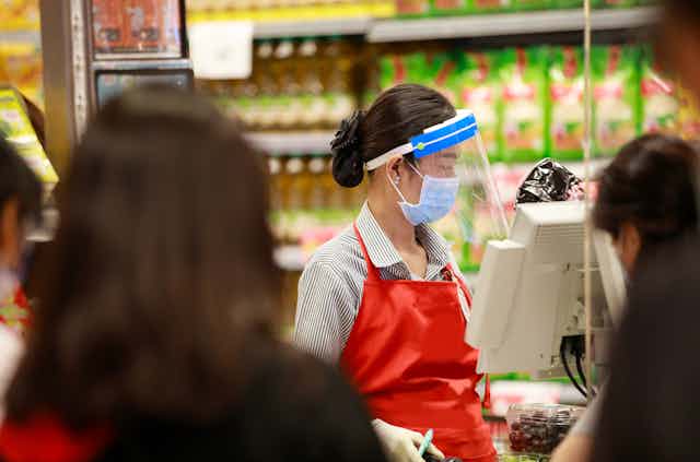 A female employee at a supermarket till, wearing a protective face mask and shield