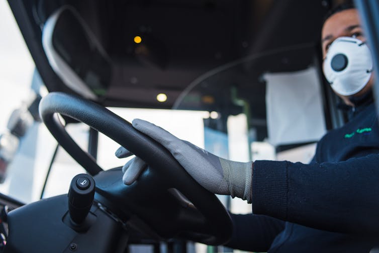 Close up of a bus driver wearing a face mask and gloves while driving