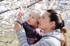 A mother and child seen looking at blossoms.