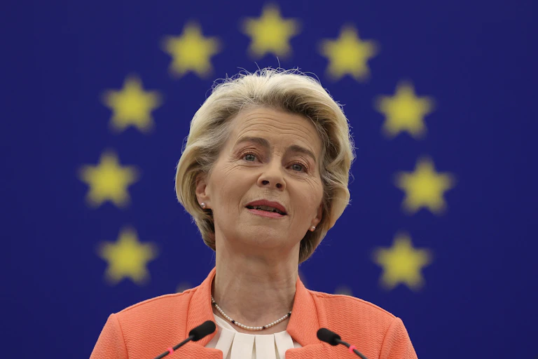 Ursula von der Leyen standing in front of an EU flag.
