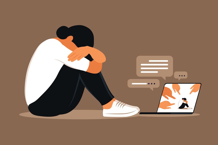 Femme déprimée assise par terre face à un ordinateur et victime de cyberharcèlement