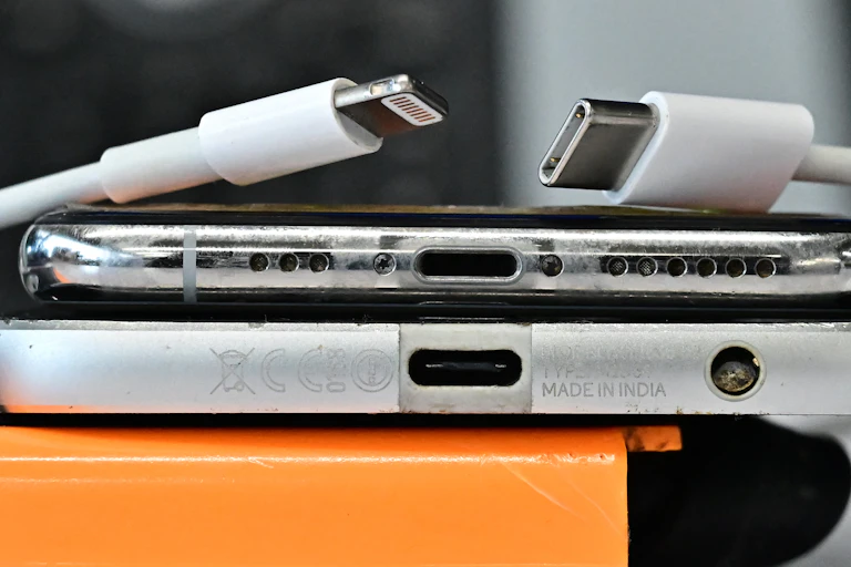 the port ends of two smartphones, one laying on the other, with two connector cables above the top phone