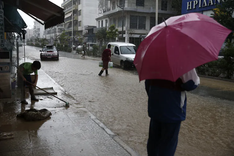 A person holds a red umbrella in a flooded city street.