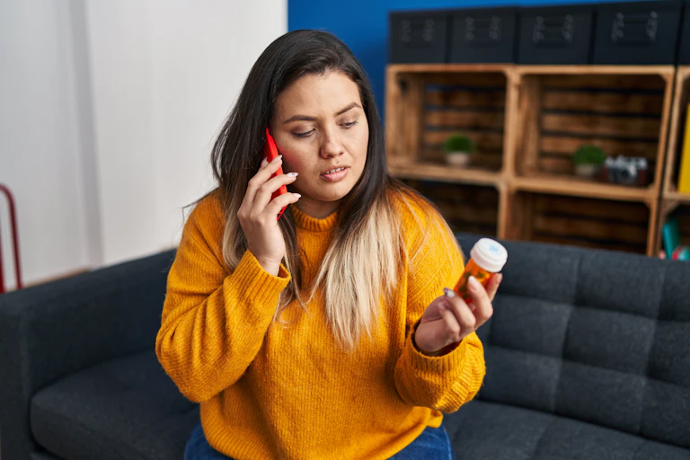 Woman talking on phone holding bottle of pills