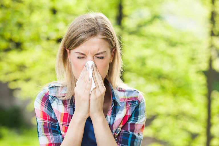 Woman blowing nose outside, trees in background