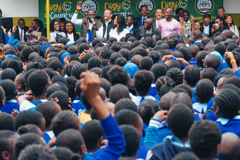School children in uniform listen to speakers at a school yard