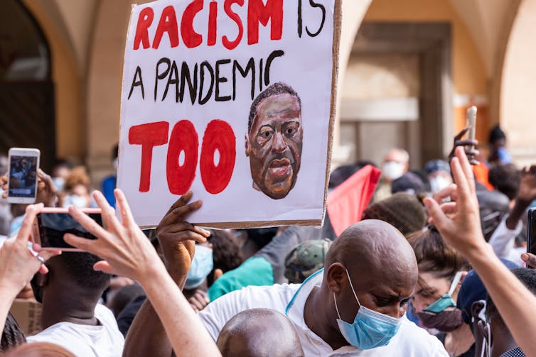 Man surrounded by crowd holding a banner with a message about racism in a peaceful protest against racism