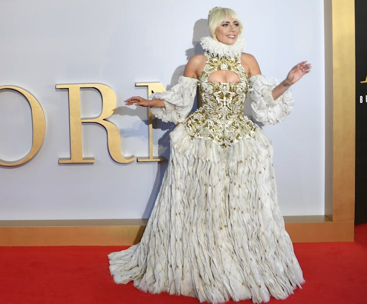 Lady Gaga on the red carpet in a gold and white dress with a ruff round the neck.