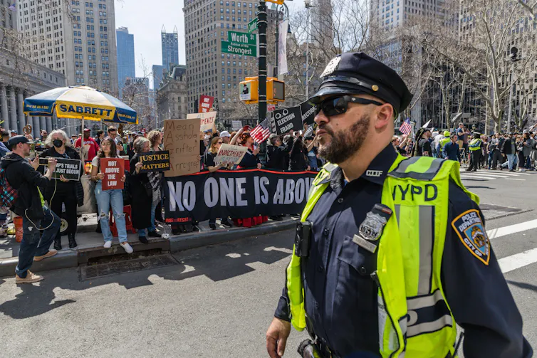 A police officer in front of a crowd of protesters ahead of former president Donald Trump's appearance in a New York court.