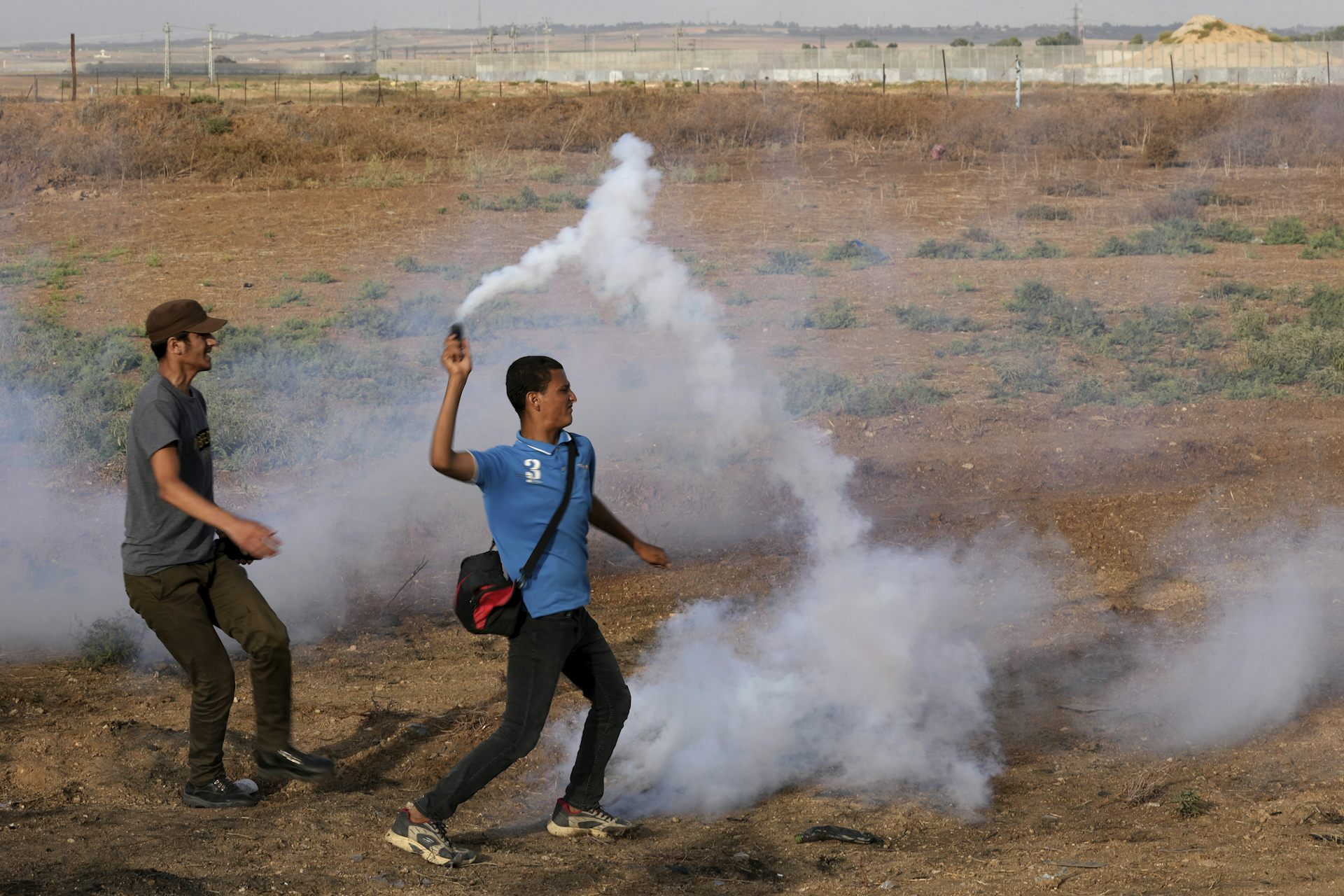 Smoke is seen as a man throws a weapon during a clash in a dusty field.