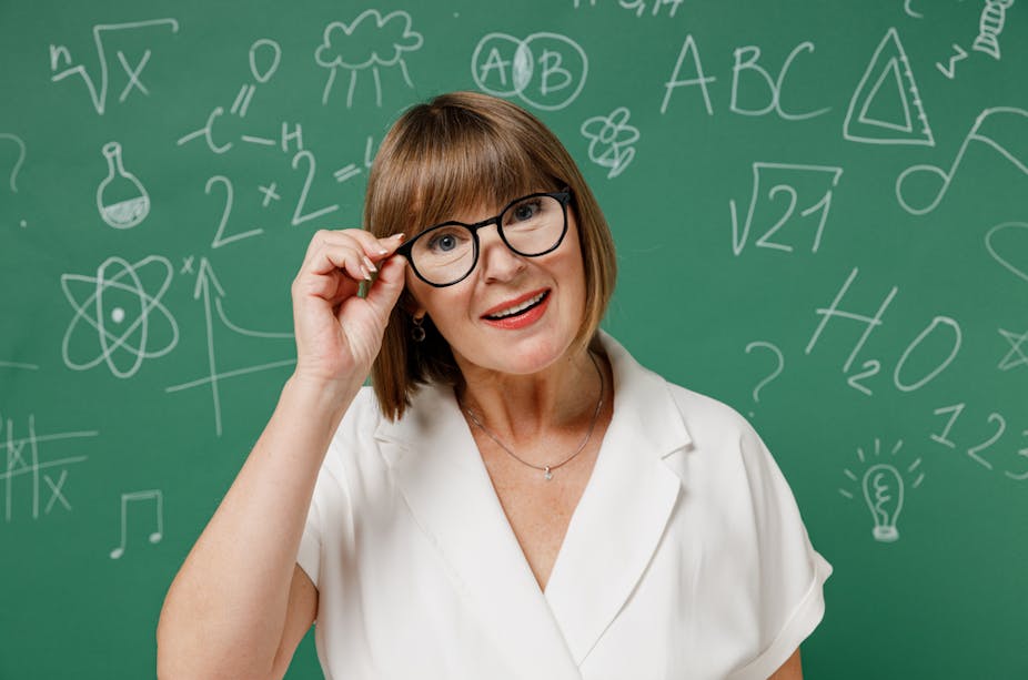 Une enseignante âgée de 55 ans devant un tableau avec des formules mathématiques