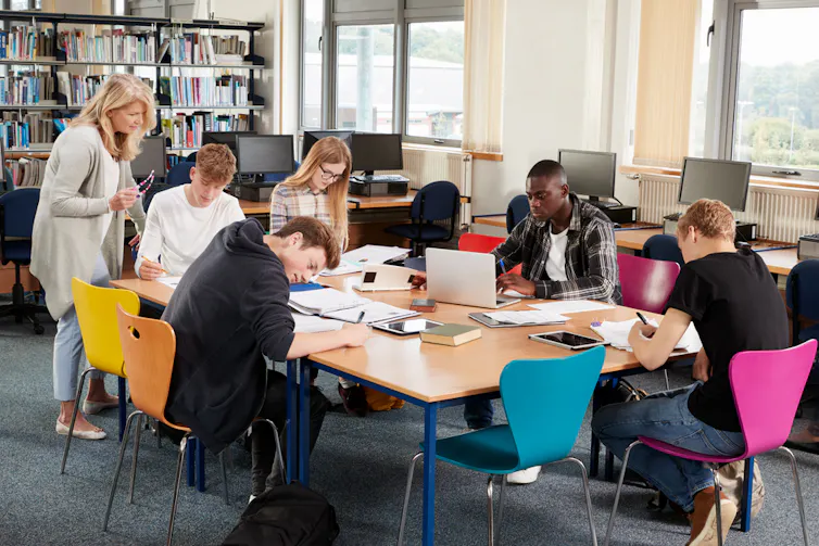 Enseignante travaillant avec un groupe de lycéens en bibliothèque
