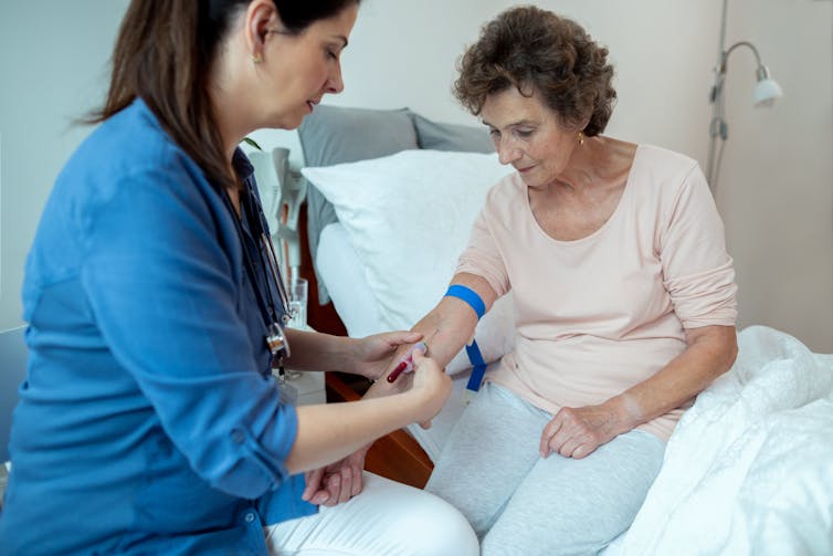 A nurse takes a blood sample from an elderly woman.