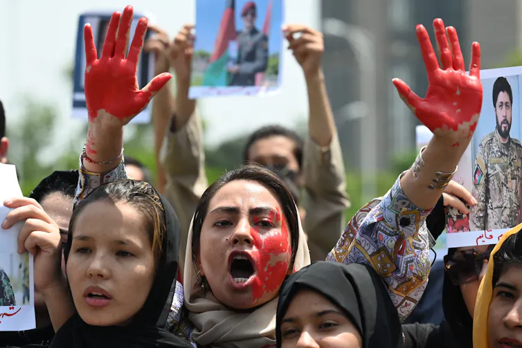 A woman with painted red hands and face stands surrounded by other protesters.