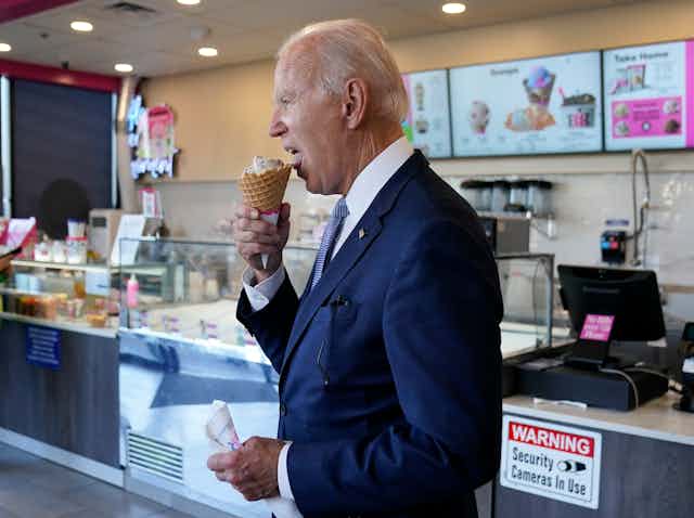 Joe Biden wears a dark navy suit and eats an ice cream cone. 