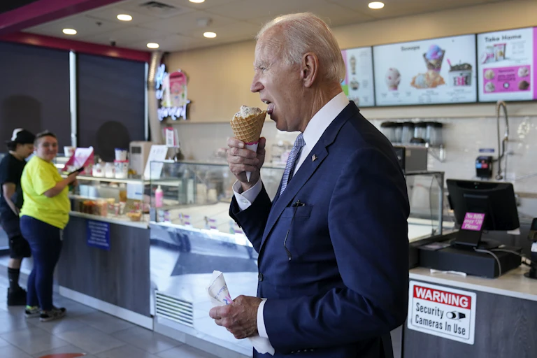 Joe Biden wears a dark navy suit and eats an ice cream cone.