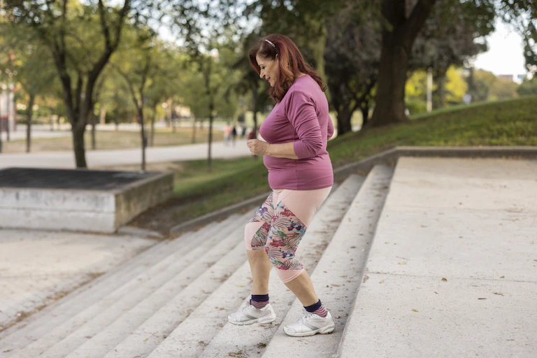 Middle-aged woman wearing athletic clothing and tennis shoes taking steps down cement stairs.