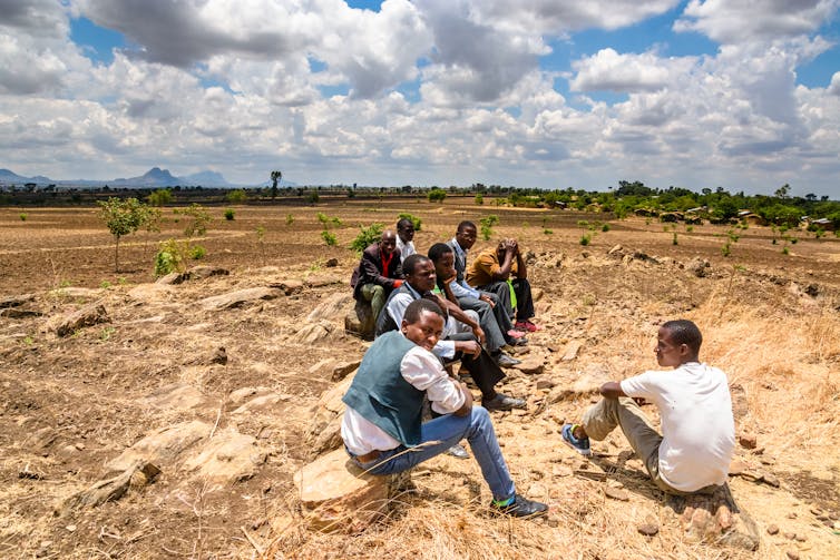 muži sedící na vrcholu malého kopce a hledící na suchá pole, která byla připravena na nadcházející deště