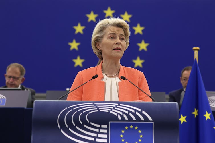 Ursula von der Leyen speaking at a podium in front of EU flag.
