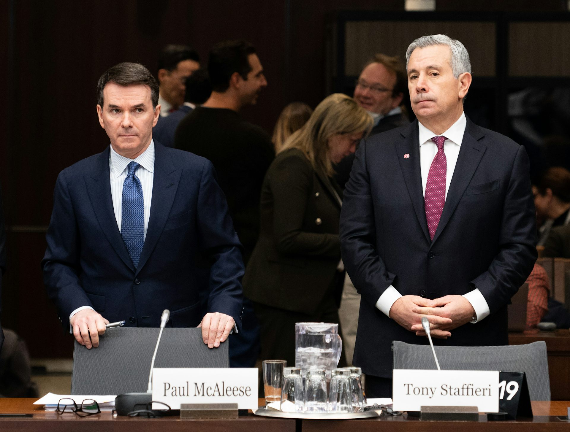 Two men in suits stand behind a table with name cards sat on top, displaying each of their names