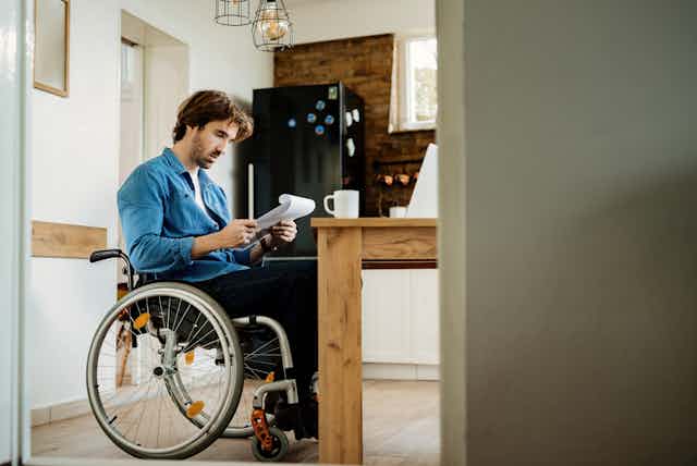 A man in a wheelchair looks at some paperwork at a kitchen table