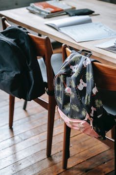 Backpacks hang on the back of chairs, behind an empty desk.