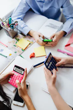 Students sit at a desk with calculators and books.
