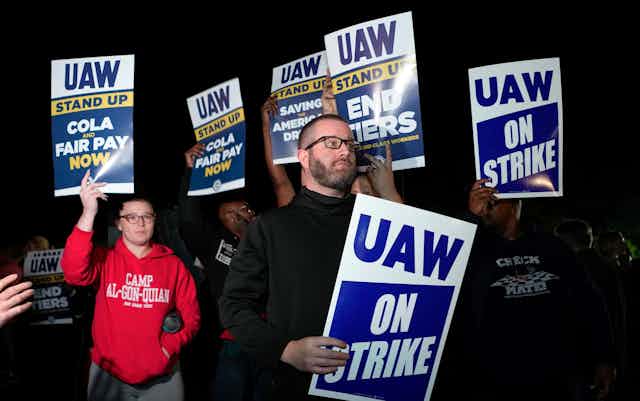 People gather at night holding signs saying 'UAW on strike.'