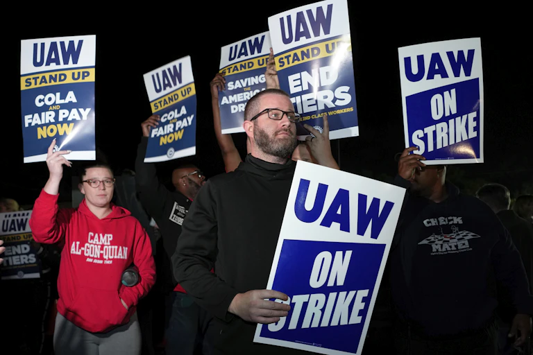People gather at night holding signs saying 'UAW on strike.'