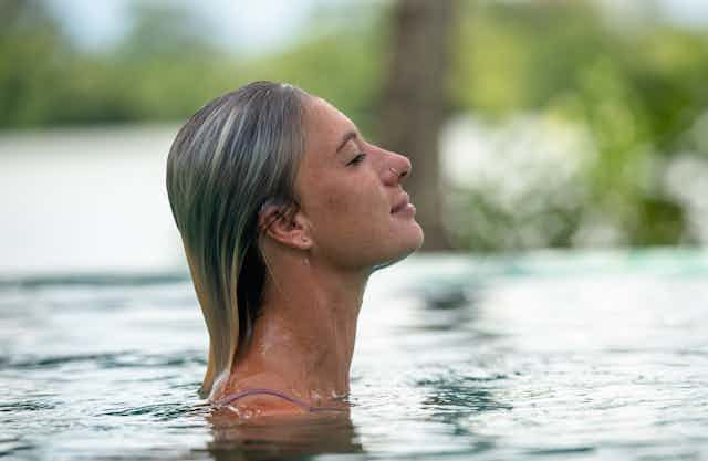 A blonde woman with wet hair emerging from a pool