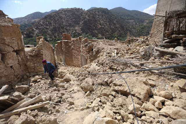 A person walks through rubble in a mountain village.