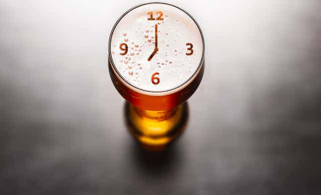 Glass of beer with clock imagery on surface.