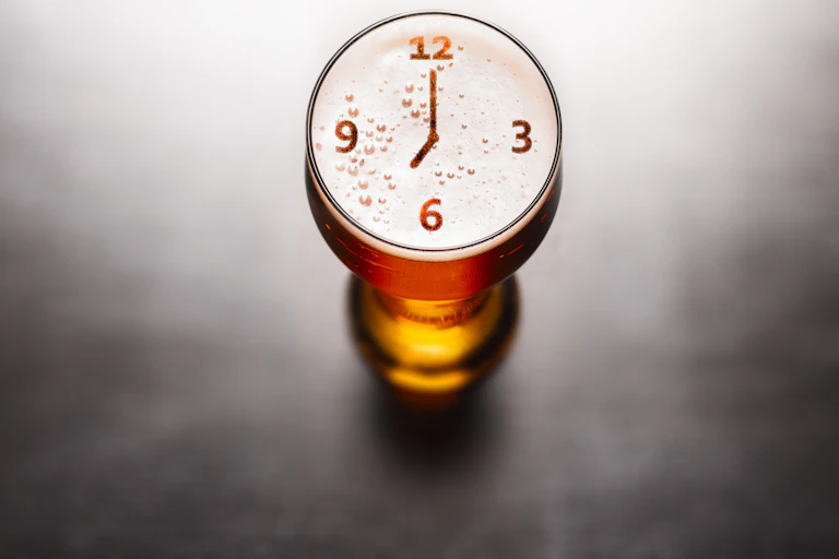 Glass of beer with clock imagery on surface.