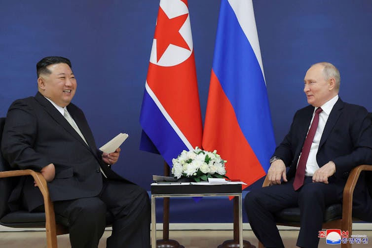 North Korean leader Kim Jong Un, left, and Russian president Vladimir Putin talk seated between the two countries' flags.