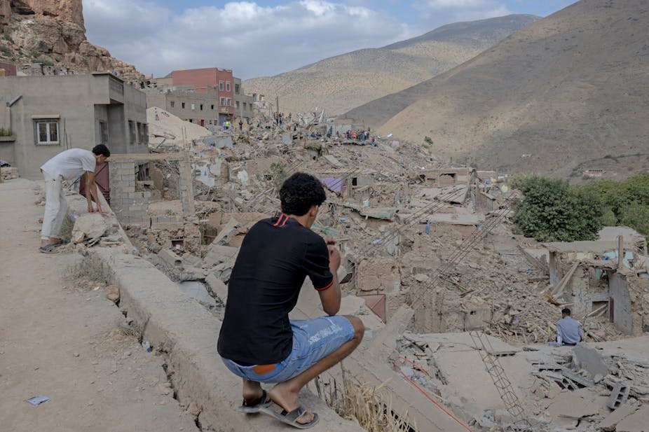 Des hommes regardent un village montagneux aux bâtiments détruits